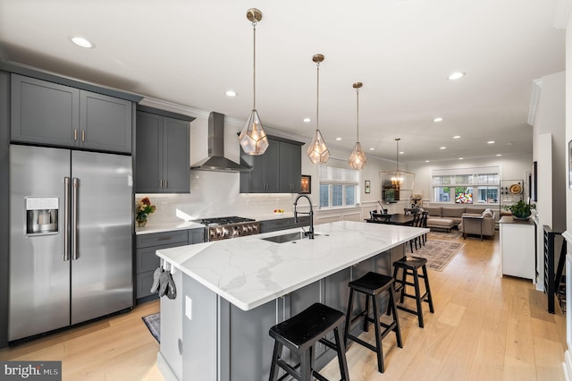 kitchen with appliances with stainless steel finishes, hanging light fixtures, wall chimney exhaust hood, and light hardwood / wood-style floors