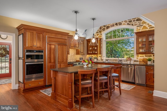 kitchen with appliances with stainless steel finishes, a center island, pendant lighting, dark wood-type flooring, and decorative backsplash