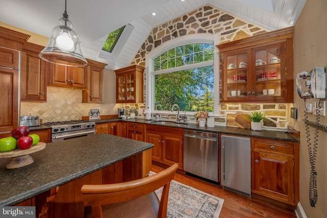 kitchen with hanging light fixtures, light hardwood / wood-style flooring, dark stone countertops, vaulted ceiling with skylight, and stainless steel appliances