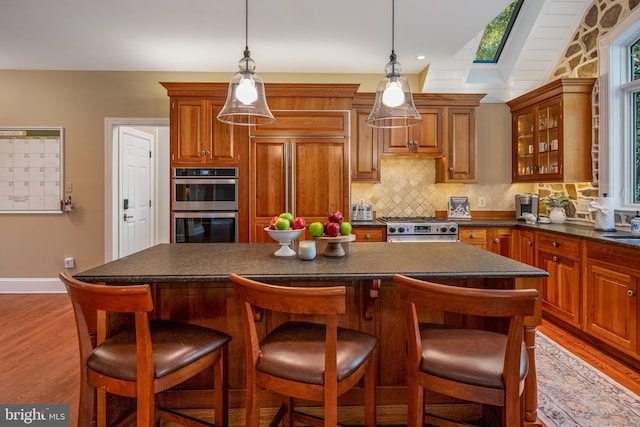 kitchen featuring a breakfast bar area, high quality appliances, light hardwood / wood-style flooring, hanging light fixtures, and lofted ceiling with skylight