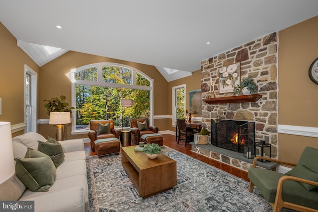 living room with a stone fireplace, wood-type flooring, and vaulted ceiling