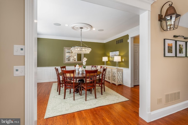 dining space with ornamental molding, a notable chandelier, hardwood / wood-style flooring, and ornate columns