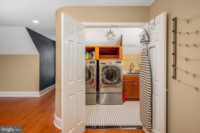 laundry area featuring sink, hardwood / wood-style floors, washing machine and clothes dryer, and cabinets