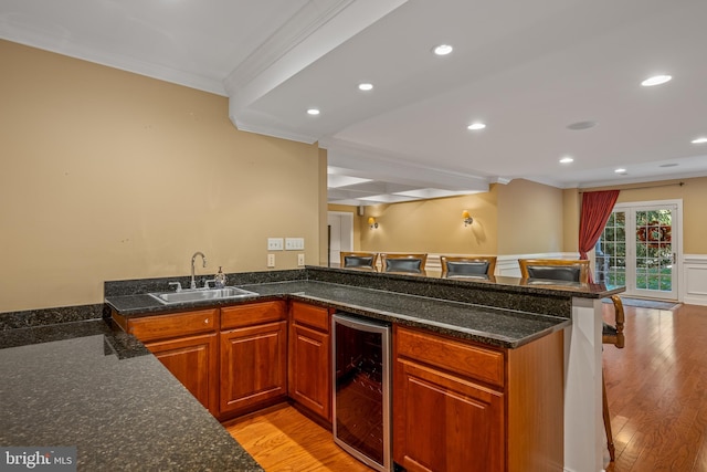 kitchen featuring kitchen peninsula, ornamental molding, sink, beverage cooler, and light hardwood / wood-style floors