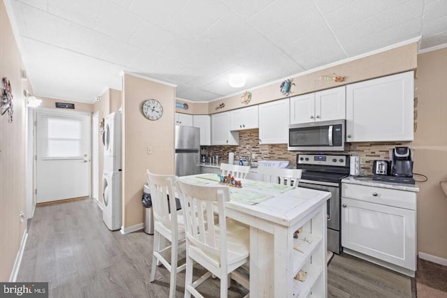 kitchen with appliances with stainless steel finishes, stacked washing maching and dryer, white cabinetry, and tile countertops