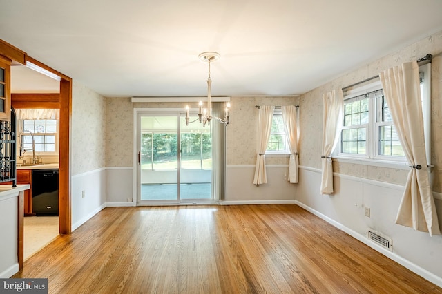 unfurnished dining area featuring a healthy amount of sunlight, sink, light hardwood / wood-style flooring, and a chandelier