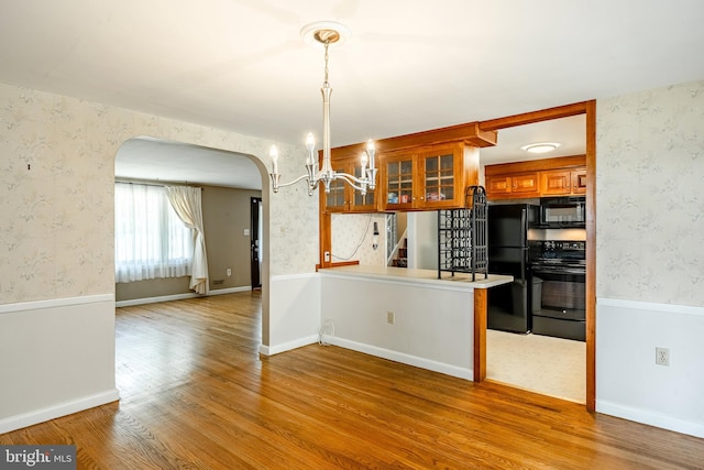 kitchen featuring light hardwood / wood-style flooring, black appliances, kitchen peninsula, an inviting chandelier, and hanging light fixtures