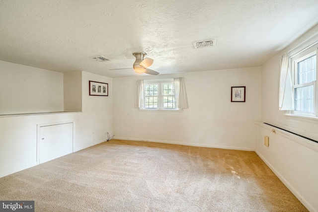 empty room featuring a textured ceiling, light colored carpet, and ceiling fan