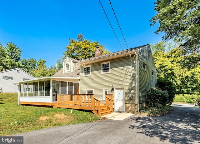 rear view of property featuring a sunroom, a deck, and a lawn