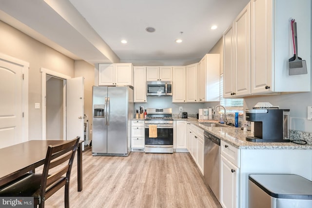 kitchen with light wood-type flooring, sink, white cabinetry, stainless steel appliances, and light stone countertops