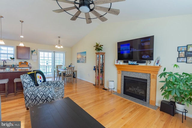 living room featuring sink, light wood-type flooring, ceiling fan with notable chandelier, and lofted ceiling