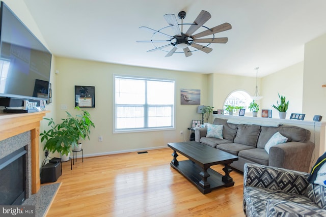 living room with ceiling fan, light hardwood / wood-style flooring, a wealth of natural light, and a high end fireplace