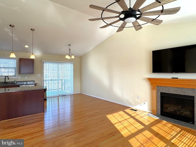 unfurnished living room with light hardwood / wood-style floors, sink, ceiling fan with notable chandelier, and vaulted ceiling