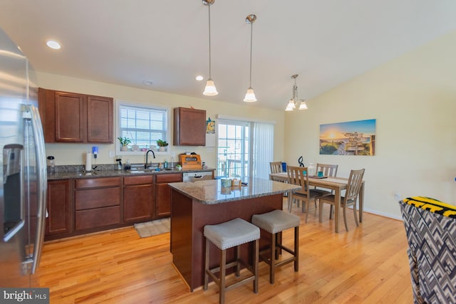 kitchen featuring hanging light fixtures, sink, stainless steel fridge with ice dispenser, a breakfast bar, and a kitchen island