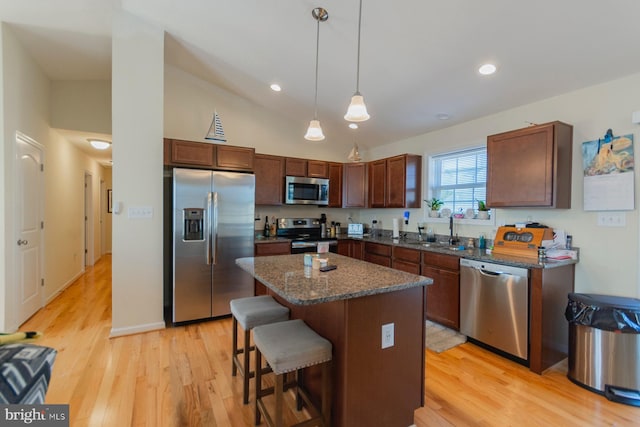 kitchen with appliances with stainless steel finishes, a center island, decorative light fixtures, light wood-type flooring, and a breakfast bar area