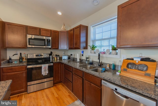 kitchen featuring vaulted ceiling, sink, light wood-type flooring, dark stone counters, and stainless steel appliances