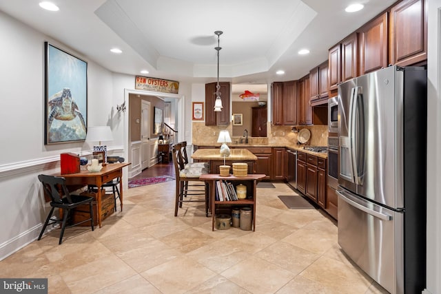 kitchen with light stone counters, decorative light fixtures, appliances with stainless steel finishes, and a tray ceiling