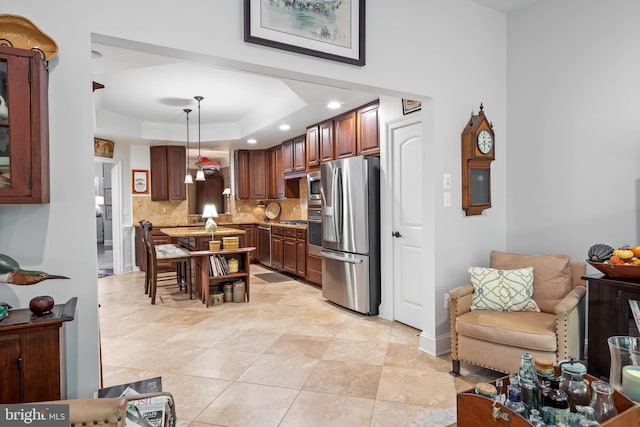 kitchen featuring light stone counters, tasteful backsplash, decorative light fixtures, stainless steel appliances, and a tray ceiling