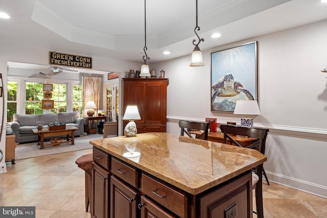 kitchen with a kitchen bar, a kitchen island, a raised ceiling, light stone countertops, and ceiling fan