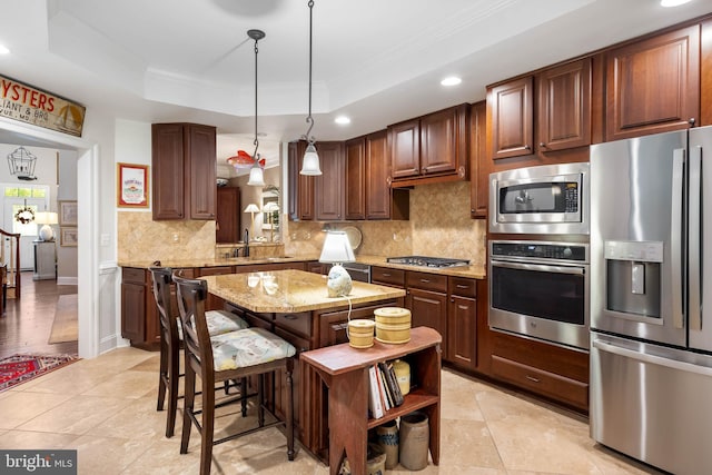 kitchen with a raised ceiling, a kitchen island, stainless steel appliances, decorative light fixtures, and sink