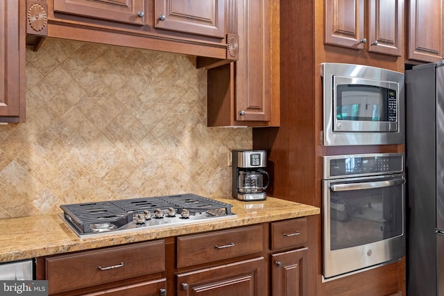 kitchen featuring stainless steel appliances, light stone counters, and backsplash