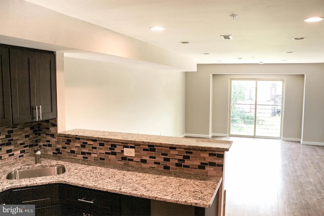 kitchen with light stone countertops, sink, tasteful backsplash, and light hardwood / wood-style flooring