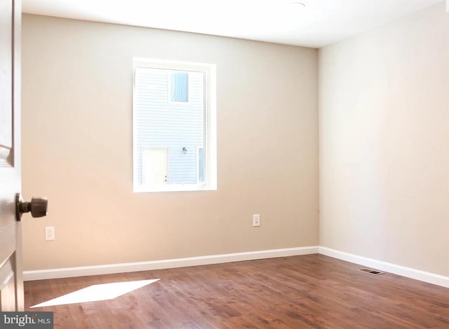 spare room with wood finished floors, visible vents, and baseboards