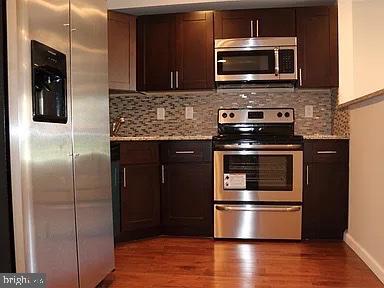 kitchen featuring dark hardwood / wood-style flooring, light stone countertops, stainless steel appliances, and decorative backsplash