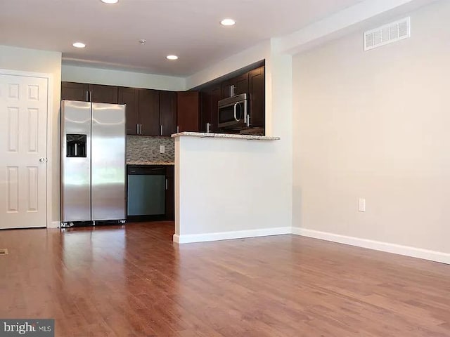 kitchen featuring backsplash, hardwood / wood-style flooring, appliances with stainless steel finishes, light stone countertops, and dark brown cabinetry