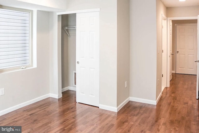 unfurnished bedroom featuring wood finished floors, baseboards, and a closet