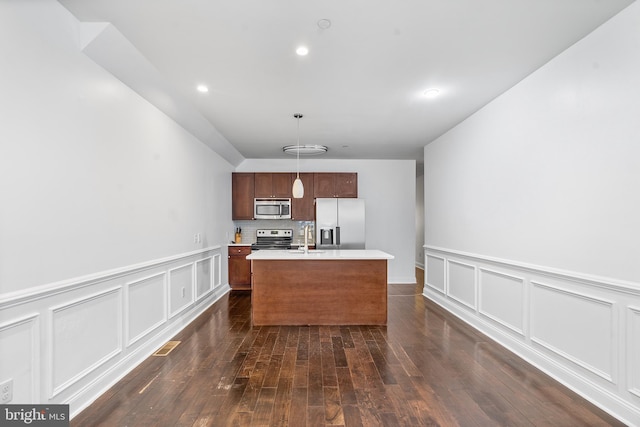 kitchen with appliances with stainless steel finishes, sink, hanging light fixtures, dark hardwood / wood-style floors, and a kitchen island with sink