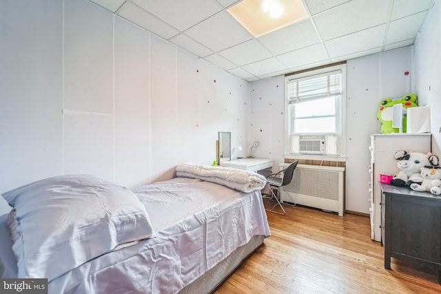 bedroom featuring light wood-type flooring, cooling unit, radiator, and a paneled ceiling