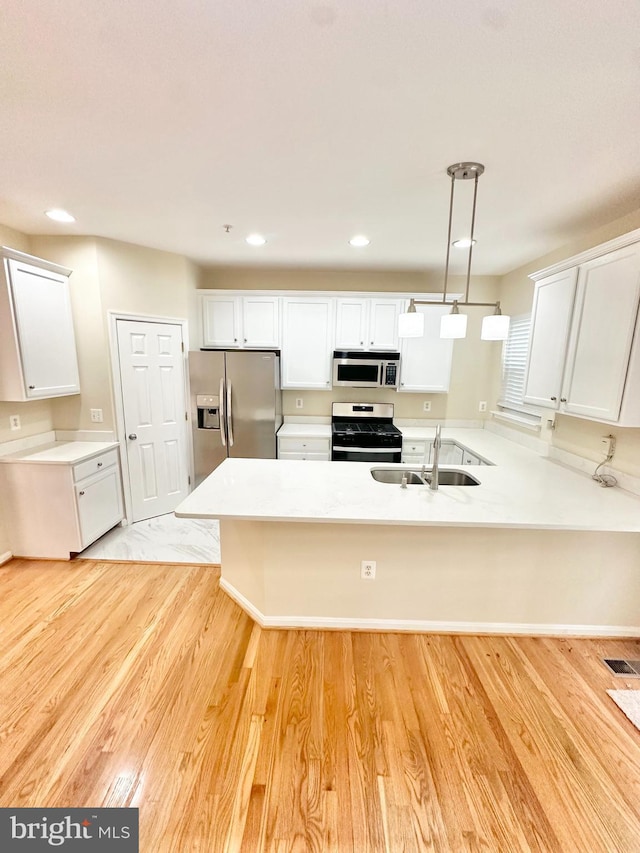 kitchen with stainless steel appliances, sink, light wood-type flooring, and hanging light fixtures