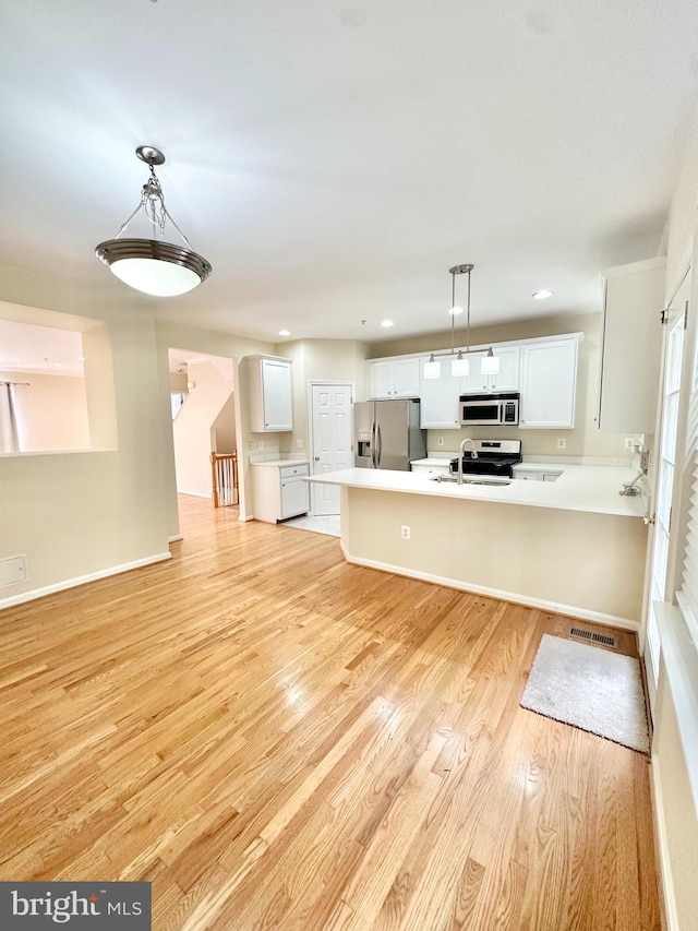 kitchen featuring light wood-type flooring, kitchen peninsula, hanging light fixtures, white cabinetry, and stainless steel appliances