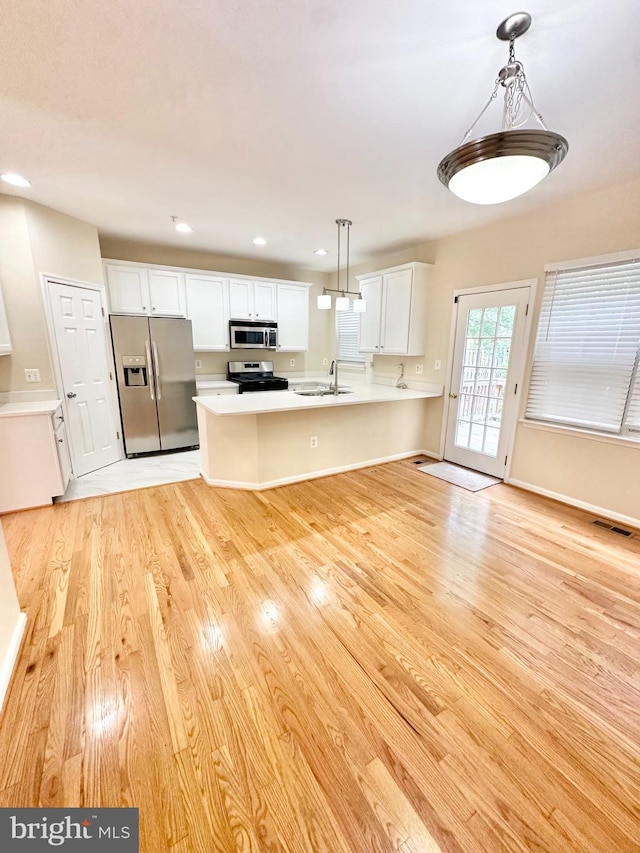 kitchen featuring white cabinets, light wood-type flooring, stainless steel appliances, sink, and decorative light fixtures