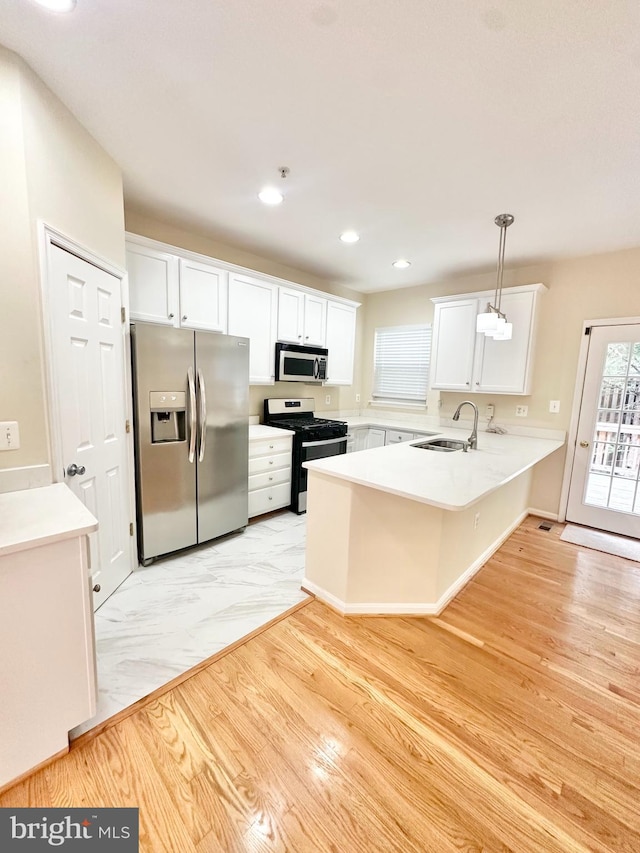 kitchen with hanging light fixtures, kitchen peninsula, sink, white cabinets, and appliances with stainless steel finishes