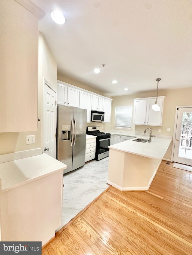 kitchen featuring kitchen peninsula, white cabinetry, stainless steel appliances, sink, and decorative light fixtures