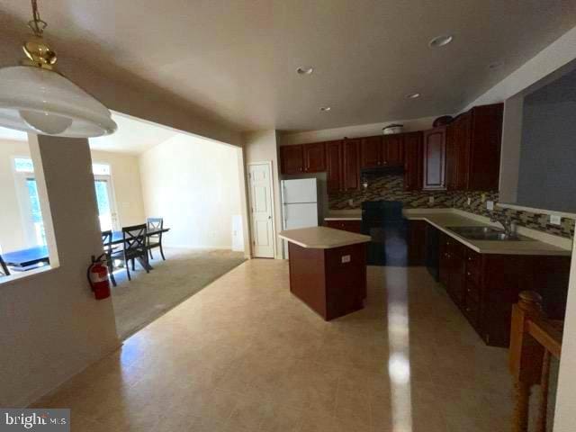 kitchen with decorative light fixtures, sink, white fridge, a kitchen island, and tasteful backsplash