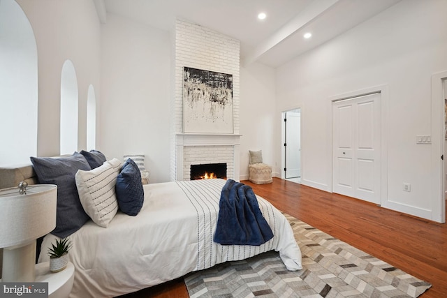 bedroom with a brick fireplace, a towering ceiling, and hardwood / wood-style flooring