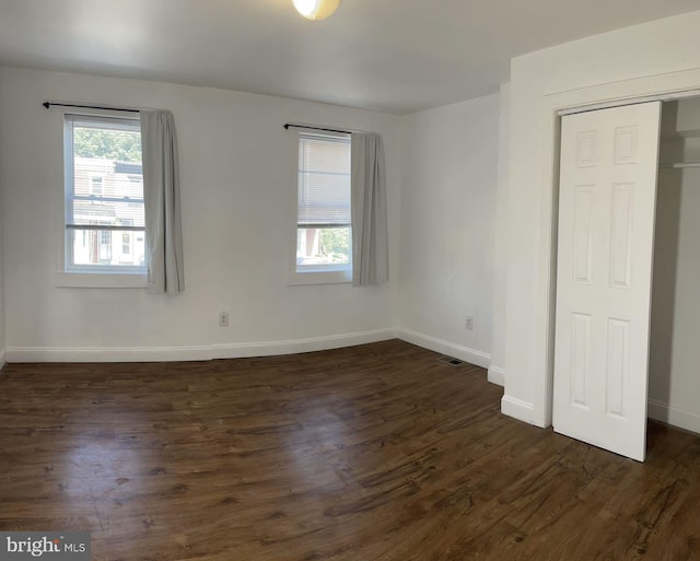 unfurnished bedroom with a closet, dark hardwood / wood-style floors, and multiple windows