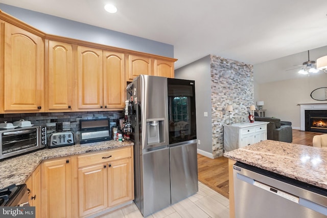 kitchen with light stone countertops, light brown cabinets, stainless steel appliances, and light hardwood / wood-style floors