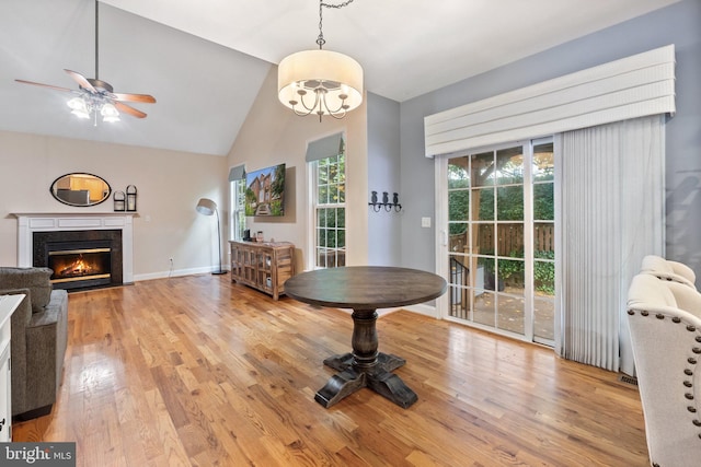 dining space with a premium fireplace, light wood-type flooring, ceiling fan with notable chandelier, and vaulted ceiling