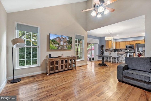 living room featuring plenty of natural light, ceiling fan with notable chandelier, high vaulted ceiling, and light hardwood / wood-style flooring