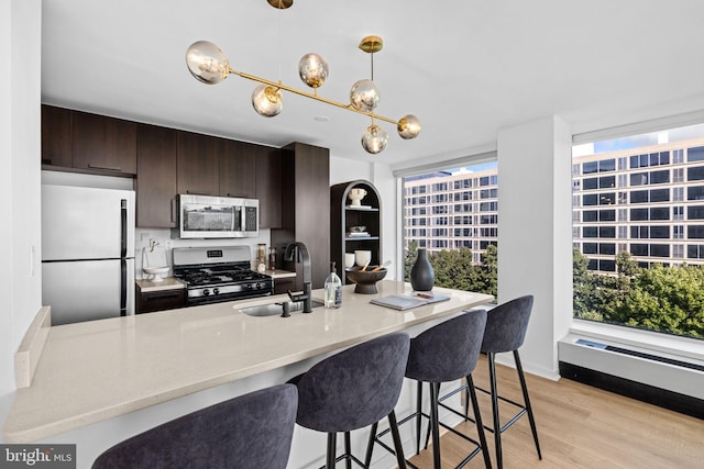 kitchen with light wood-type flooring, sink, a kitchen breakfast bar, appliances with stainless steel finishes, and dark brown cabinetry