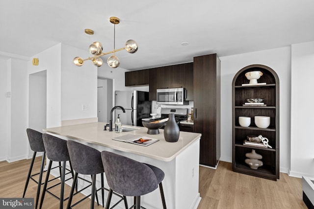 kitchen with dark brown cabinetry, stainless steel appliances, a kitchen breakfast bar, a notable chandelier, and light hardwood / wood-style floors