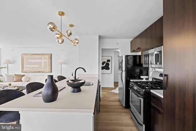 kitchen with pendant lighting, gas range, dark brown cabinets, light hardwood / wood-style flooring, and sink