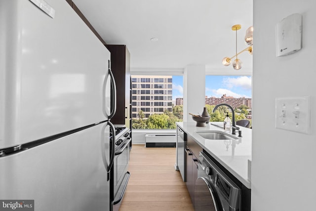 kitchen featuring pendant lighting, light stone counters, sink, light hardwood / wood-style flooring, and appliances with stainless steel finishes