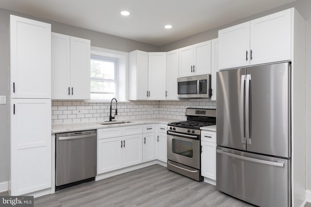 kitchen with appliances with stainless steel finishes, sink, white cabinetry, and light hardwood / wood-style flooring