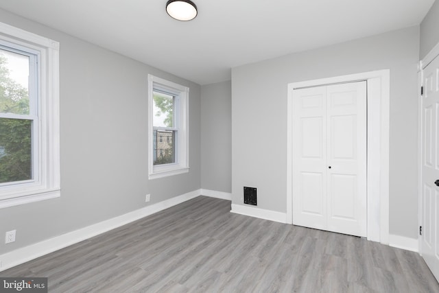 unfurnished bedroom featuring a closet, light hardwood / wood-style floors, and multiple windows