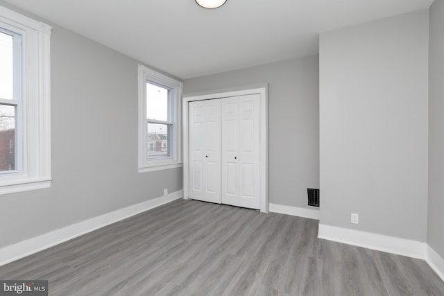 unfurnished bedroom with light wood-type flooring, a closet, and multiple windows